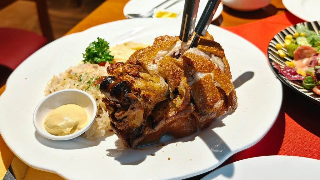 Delicious crispy pork knuckle with mustard, rice, and salad served in an ambient restaurant setting.